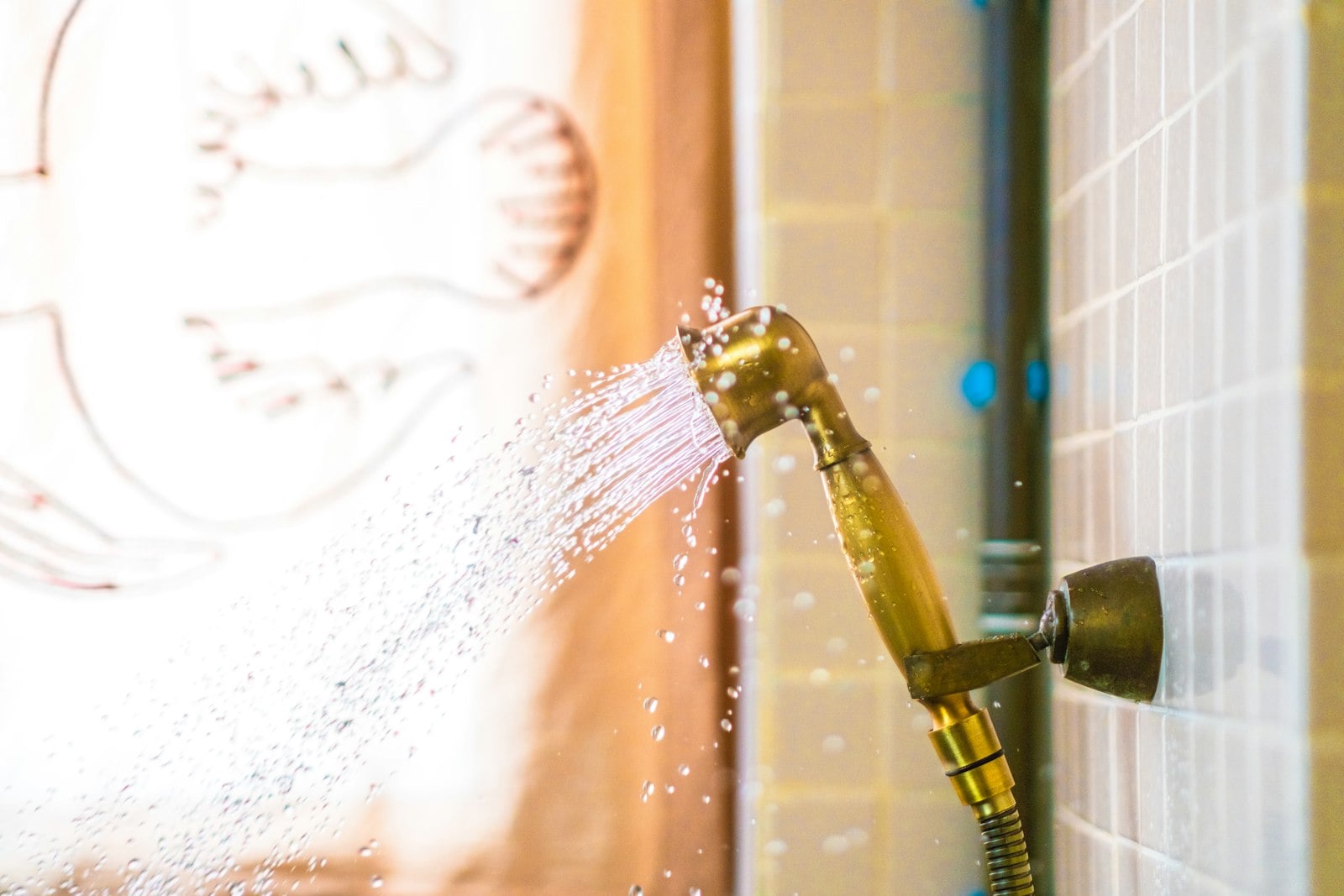 Hand shower spraying water against a tiled wall